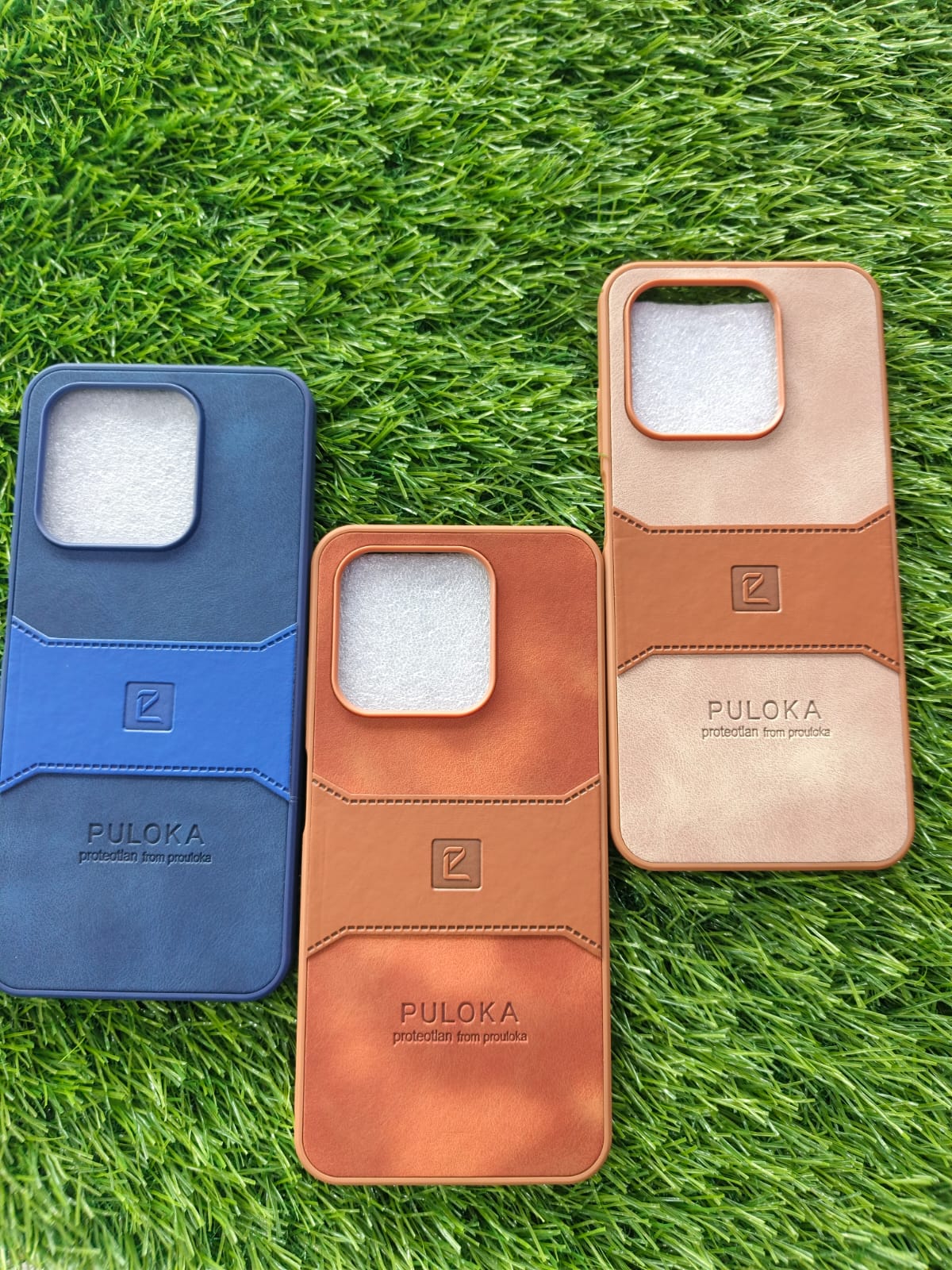 Three phone cases in blue, brown, and beige on grass, Leather touch square cut camera case for Infinix Hot 50i and Smart 9